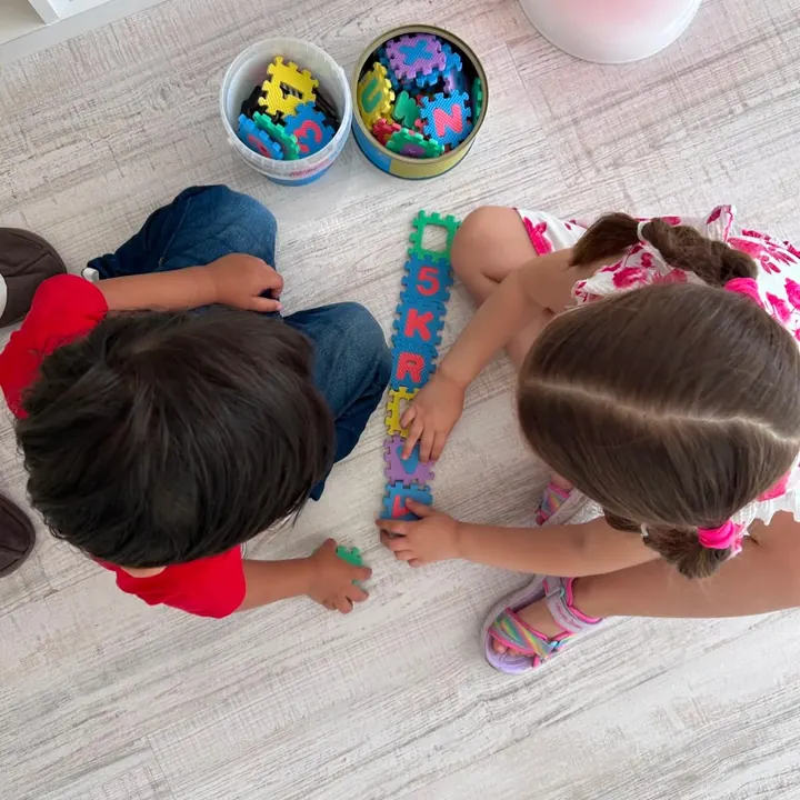Doi copii care construiesc împreună un șir de piese colorate pe covor